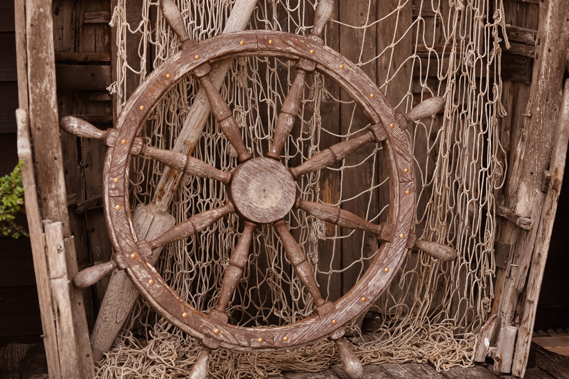 Stare drewniane koło sterowe z ośmioma użebrowaniami opierające się o sieć rybacką i postarzałe drewno