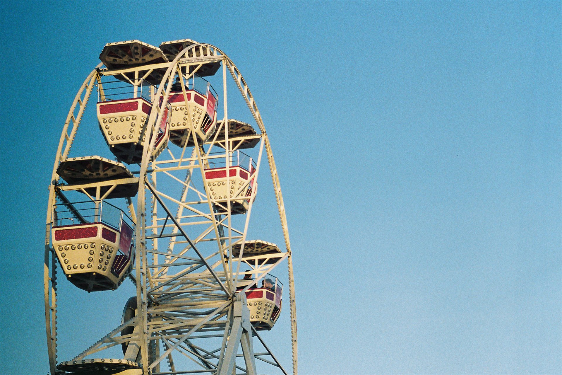 białe diabelskie koło z czerwonymi kabinami na tle jasnoniebieskiego nieba