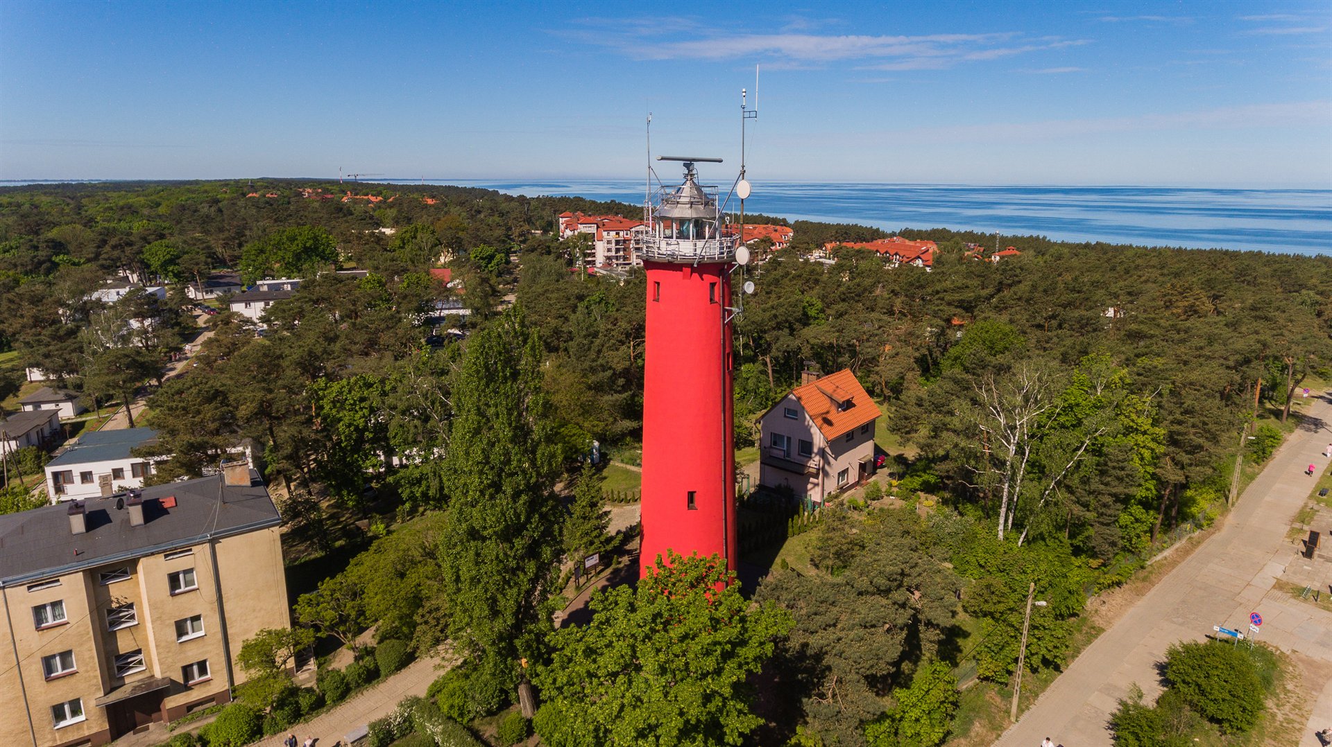 Wysoki czerwony latarnia morska otoczona sosnowym lasem i domami przy wybrzeżu, widok z lotu ptaka