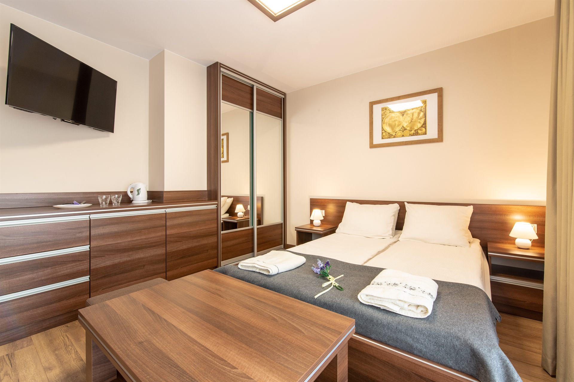 Jasny pokój z podwójnym łóżkiem, drewniane meble, lampa nocna, ręczniki i gałązka lawendy na narzucie