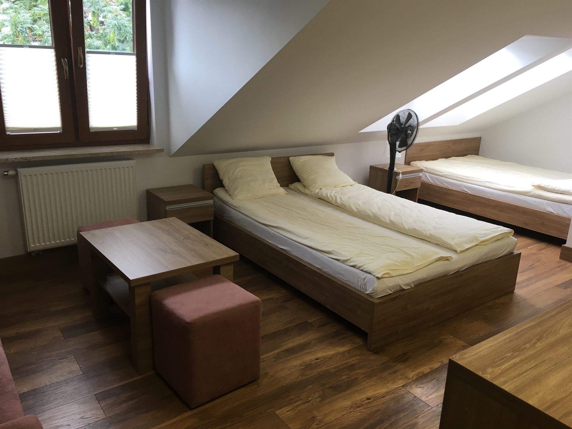 Sypialnia na poddaszu z trzema pojedynczymi łóżkami, drewnianymi meblami i stojącym wiatrakiem