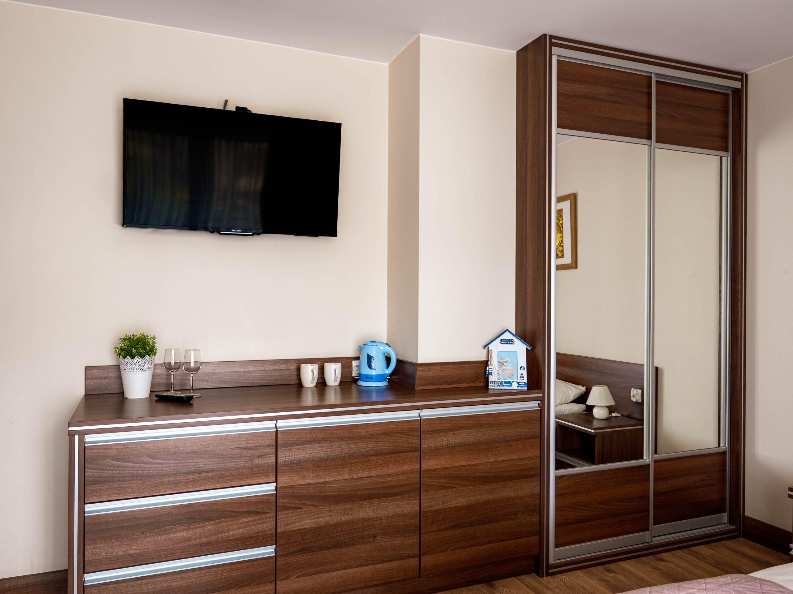 Pokój hotelowy z telewizorem, drewnianą komodą i szafą z lustrzanymi drzwiami