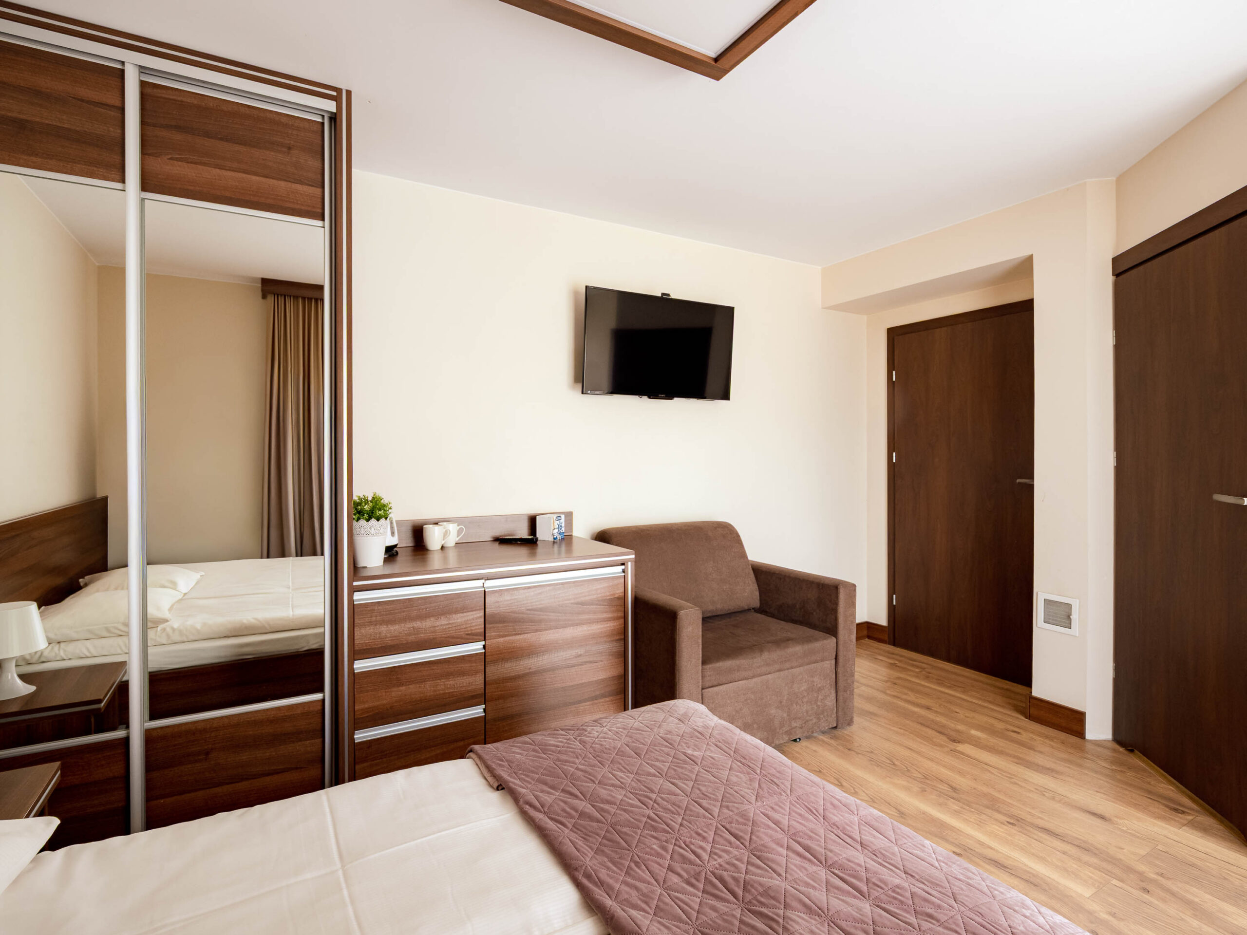 Nowoczesny pokój hotelowy z łóżkiem, szafą, fotelem i telewizorem na ścianie
